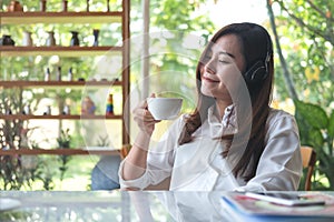 Asian woman close her eyes and listening to music with headphone while drinking coffee with feeling happy and relax in cafe with g