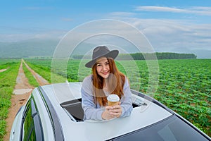 Asian woman with coffee and standing out of car sunroof. Relaxing and freedom with spring time. Young tourist travel alone