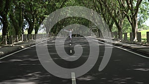 Asian woman in a colored stylish dress with turban walks and dance along the asphalt road under shady trees in the park.