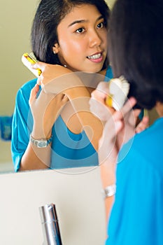 Asian woman combing hair in bathroom mirror