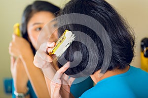 Asian woman combing hair in bathroom mirror