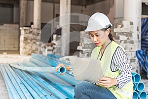 Asian woman construction engineer using notebook computer for checking the PVC pipe