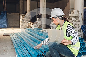 Asian woman construction engineer using notebook computer for checking the PVC pipe