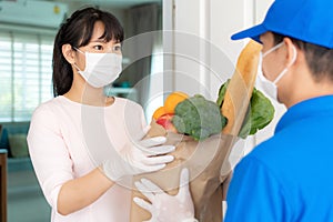 Asian woman costumer wearing face mask and glove receive groceries bag of food, fruit, vegetable from delivery man in front of the