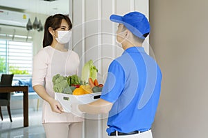 Asian woman costumer wearing face mask receive groceries box of food, fruit and vegetable from delivery man   in front of the