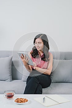 Asian woman on the couch at home doing online shopping, so comfortable, in fashioanble white outfit, so nice light design