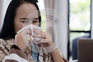 An Asian woman covered with blanket blowing running nose got fever caught cold sneezing in tissue sit on sofa