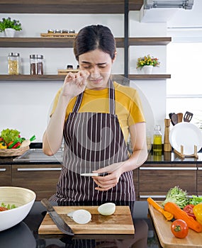 Asian woman crying while holding a piece of onion. Young housewife slices onion into pieces on a wooden chopping board. Morning