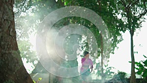 An Asian woman dancing near the smoke from the burning trash while wearing a traditional pink dress inside the forest