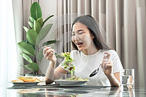 Asian woman dip fresh vegetable salad with a fork to eating healthy meal on the table in dining room at home