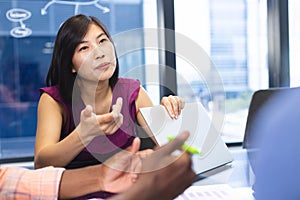Asian woman discussing with colleague, both using laptops in a modern business office