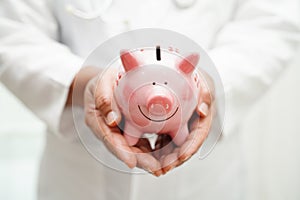 Asian woman doctor holding piggy bank, cost of treatment or education concept