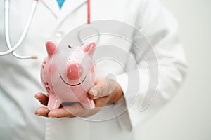 Asian woman doctor holding piggy bank, cost of treatment or education concept