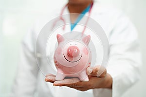 Asian woman doctor holding piggy bank, cost of treatment or education concept