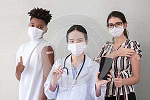 Asian woman doctor holding showing smart phone and syringe with mask and stethoscope. Vaccinated people standing back