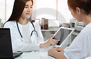 Asian woman doctor holding tablet with isolated blank screen while consulting patient in medical consultation room