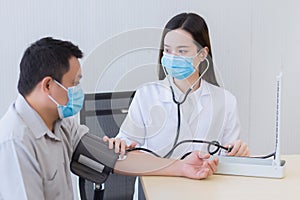 Asian woman doctor uses stethoscope and a blood pressure motoring to measure blood pressure of the man patient. In healthcare