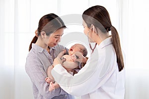 Asian woman doctor using stethoscope examining  on newborn baby in mother`s arms. Mom holding adorable infant get sick crying in
