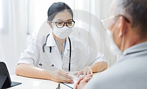 Asian woman Doctor wear eyeglasses and face mask giving advice to Elderly patient
