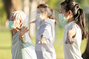 Asian woman is doing exercise activity for the old elderly and child girl,family workout and wearing medical mask outdoor after