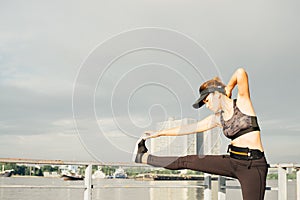 asian woman doing stretching exercises outdoors along city sidewalk in summer warm light