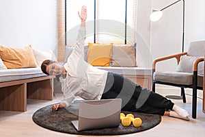 Asian woman doing stretching yoga exercise, raise arm and makes a side plank pose while using laptop to conducting