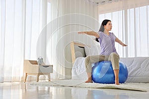 Asian woman doing yoga exercise with fitness ball in her bedroom as a result of social distancing and quarantine period