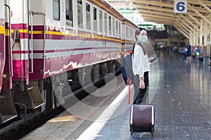 Asian woman drag her bag to travel or come back to home by train at station while she wears medical face mask.