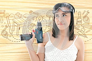 Asian woman dressed in white top holding a cordless electric drill on wood background