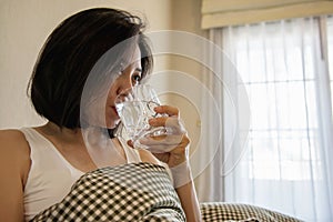 Asian woman drink water after wake up in the morning sitting on a bed