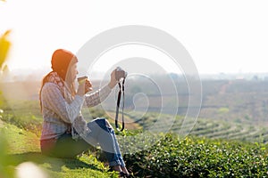 Asian Woman drinking beverage tea and take a photo, relaxing and sitting outdoor in the tea plantation