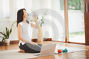 Asian woman drinking from her water bottle while practicing yoga at home