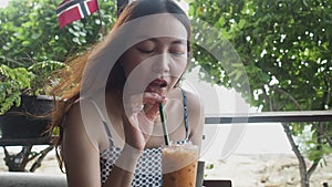 Asian woman drinking juice at beach bar. female feeling happy after having refreshment drink.