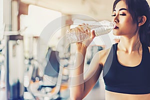 Asian woman drinking pure drinking water for freshness after workout or exercise training in fitness gym with fitness equipment b