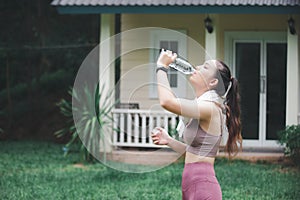 Asian woman drinking water on front yard after jogging  healty and sport concept