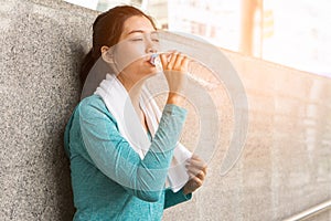 Asian woman drinking water to rehydrate to avoid heat stroke after running outdoors in the summer
