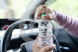 Asian woman driver holding bottle for drink water while driving a car. Plastic hot water bottle cause fire