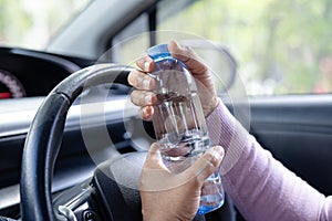 Asian woman driver holding bottle for drink water while driving a car. Plastic hot water bottle cause fire