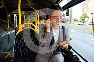 Asian woman in earphones using cellphone while traveling in bus