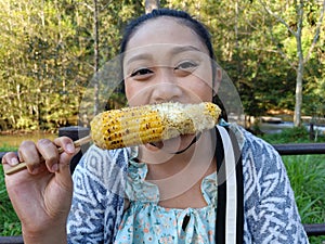 Asian woman eating delicious grilled corn, appetizer, picnic time