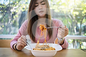 Asian woman eating instant noodles with fork on blurred background of restaurant