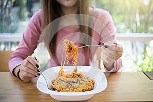 Asian woman eating instant noodles with fork on blurred background of restaurant