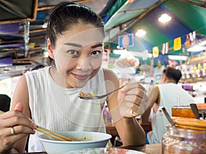 Asian woman eating noodle in Thai local restaurant.