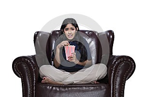 Asian woman eating popcorn while sitting on the couch with a scared expression