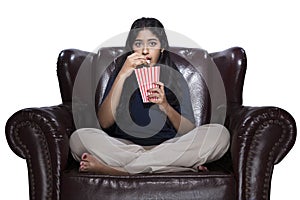 Asian woman eating popcorn while sitting on the couch with a scared expression