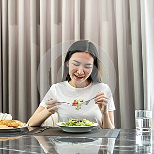 Asian woman eating vegetable salad mix with tomato for healthy meal on the table in dining room at home
