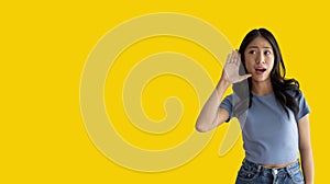 Asian woman eavesdropping or overhearing secret conversation isolated on yellow background