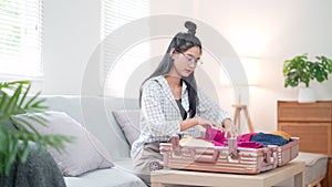 Asian woman efficiently rolls and packs clothes compactly, preparing