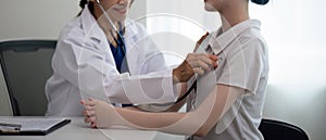 Asian woman elderly doctor at hospital taking care of young woman. Doctor measure heart rate by stethoscope on older