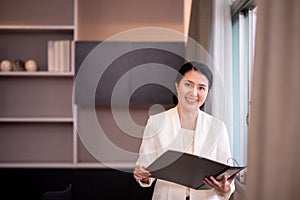 Asian woman employee in white suit holding file folder at workplace
